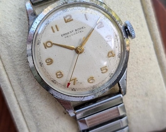 May include: A vintage Ernest Borel Neuchâtel wristwatch with a round silver-toned case, a textured off-white dial, gold-coloured Arabic numerals, and matching hands. The watch features a red-tipped second hand and a flexible silver-tone metal band.