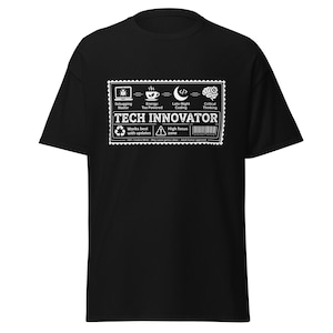 May include: Black t-shirt with a white graphic that reads "TECH INNOVATOR." The graphic includes icons for debugging, tea, coding, and critical thinking. The shirt also has the text "Works best with updates" and "High focus zone."