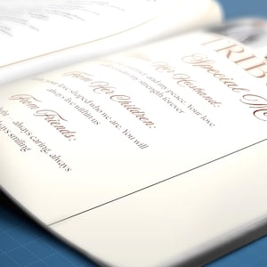 May include: An open book with a special message titled "Tributes". The text is in a brown script font on a cream-colored page. The message includes phrases like "From Her Husband" and "From Friends". The background is a blurred blue.