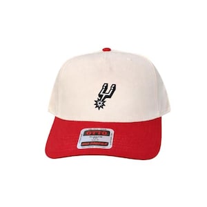 May include: A baseball cap with an off-white crown and a red brim. The front features a black embroidered spur logo. A rectangular sticker on the brim displays the text OTTO CLASSIC FIT MID PROFILE in black and red lettering on a white background.