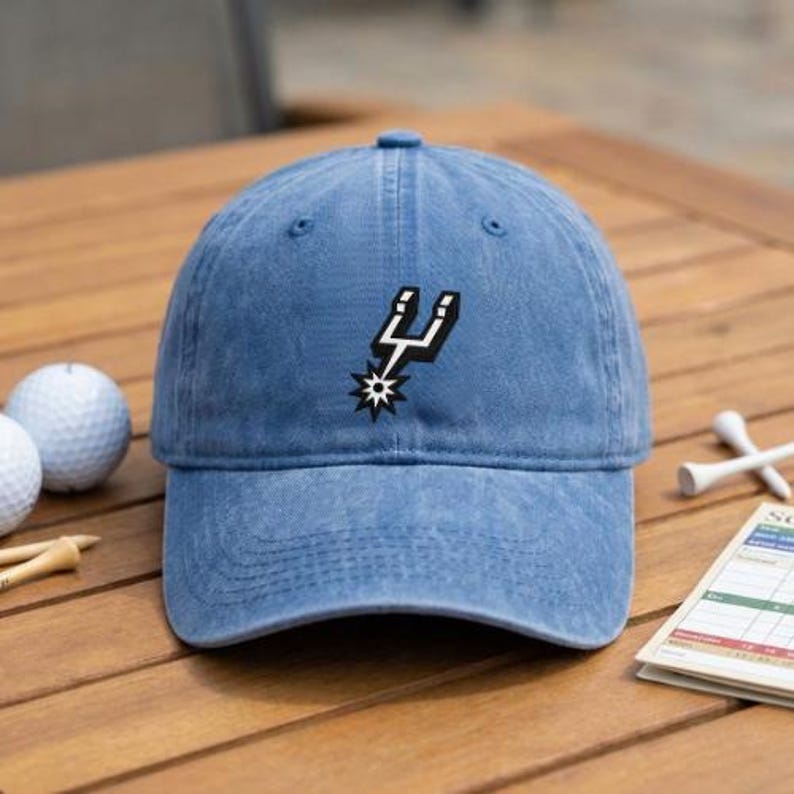 May include: A blue baseball cap with a distressed finish featuring the San Antonio Spurs logo embroidered in black and white on the front center. The cap has a curved brim and a structured crown with eyelets for ventilation.
