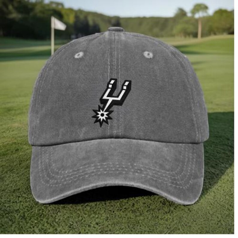 May include: A charcoal gray baseball cap featuring an embroidered San Antonio Spurs logo on the front. The cap has a curved brim, a six-panel construction with stitched eyelets, and a structured crown, showcasing the black and white spur emblem.