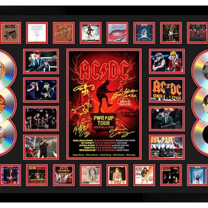 May include: A framed AC/DC display, featuring a central poster with the band's logo and tour details, surrounded by images and silver CDs. The frame is black with red detailing.