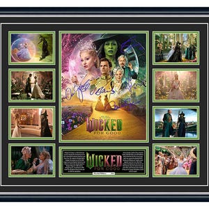 May include: Framed artwork featuring scenes from the musical "Wicked," with a central poster and smaller images around it. The artwork includes the text "Wicked For Good" and several signatures. The frame is black.