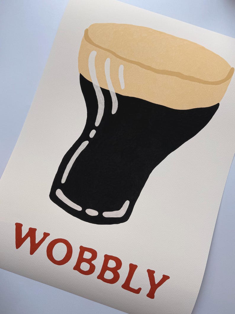 May include: A print featuring a stylized illustration of a pint of stout. The glass is black with a tan head and white foam drips. The word "WOBBLY" is printed in red at the bottom of the image.