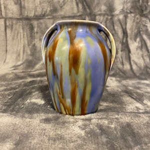 Könnte beinhalten: Eine Keramikvase mit zwei Henkeln und einer glatten, glänzenden Oberfläche. Das Design zeigt ein verlaufendes Glasurmuster in den Farben Kornblumenblau, Salbeigrün und tiefem Kastanienbraun, das eine vertikale, fließende Optik erzeugt.