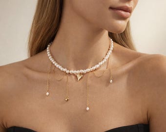 May include: A pearl necklace with a gold heart pendant and dangling gold chains. The necklace features small gold charms and pearls. The jewelry is worn on a person's neck and chest.