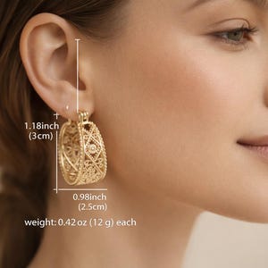 May include: Gold-toned filigree hoop earrings. Each earring is 1.18 inches (3 cm) long and 0.98 inches (2.5 cm) wide, weighing 0.42 oz (12 g). The earrings feature an openwork design with intricate patterns, showcasing a delicate and ornate style.