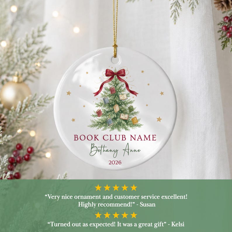 May include: A round white ceramic ornament featuring a green Christmas tree decorated with small books and a red ribbon bow at the top. The text reads BOOK CLUB NAME, Bethany Anne, and 2026 in red and black script, suspended by a gold string.