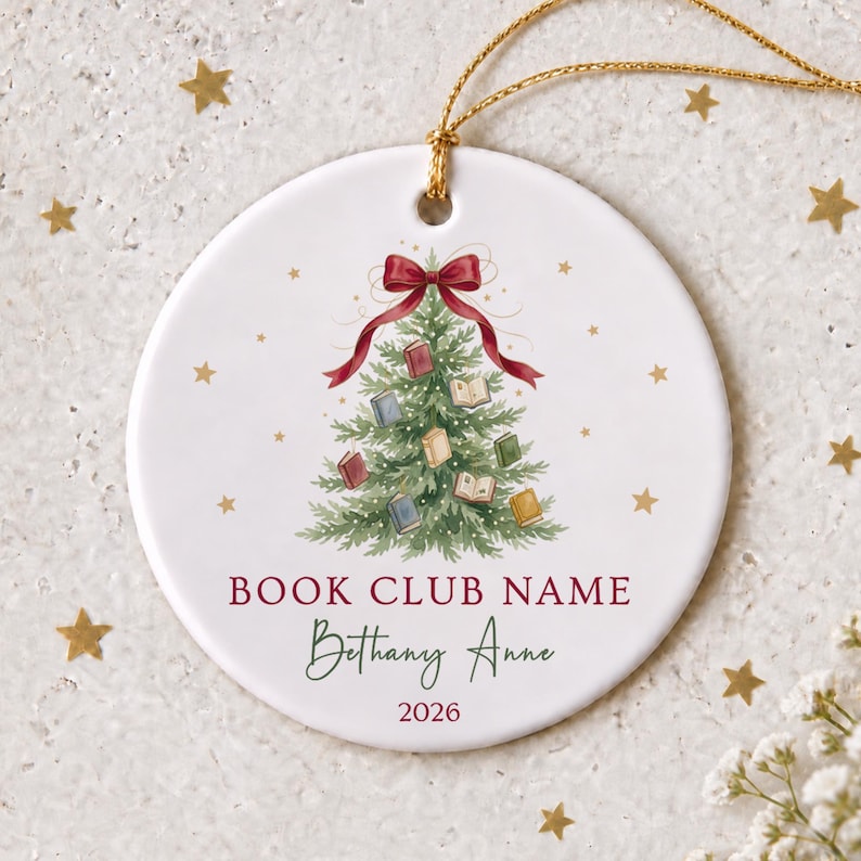 May include: A round white ceramic ornament featuring a green Christmas tree decorated with small colorful books and a red bow at the top. The text reads BOOK CLUB NAME, Bethany Anne, and 2026. A gold string is attached for hanging the ornament.