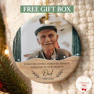 May include: A round ceramic memorial ornament featuring a photograph of an elderly man wearing a flat cap. The lower portion has a wood grain texture with the text: FOREVER LOVED. FOREVER MISSED. FOREVER IN OUR HEARTS, Dad, and 1945-2026.