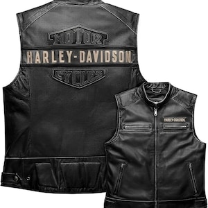 Könnte beinhalten: Eine schwarze Lederweste mit Frontreißverschluss, zwei Brusttaschen und zwei unteren Taschen. Auf der Rückseite befindet sich ein großes geprägtes Harley-Davidson Motor Cycles Logo. Ein kleines Harley-Davidson Abzeichen ist auf der Brust.