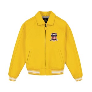 May include: A bright yellow zip-up jacket featuring a classic collar, long sleeves, and ribbed cuffs and hem with white stripes. On the left chest, there is a patch displaying the text AVIREX above a shield graphic with red and white stripes.