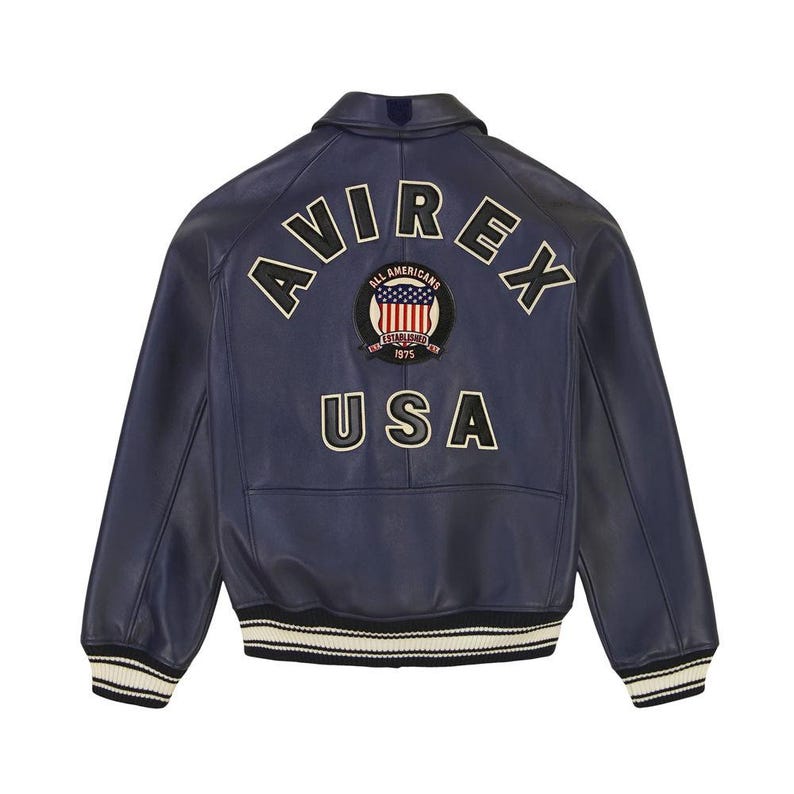 May include: A navy blue leather varsity jacket featuring the text AVIREX and USA in cream-colored lettering on the back. A circular patch in the center displays an American flag graphic with the text ALL AMERICANS ESTABLISHED 1975. The jacket has striped ribbed cuffs and hem.