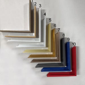 Könnte beinhalten: Eine Sammlung von zehn Bilderrahmen-Ecken in verschiedenen Farben und Ausführungen. Die Rahmen umfassen Brauntöne, Weiß, Silber, Gold, Schwarz, Blau und Rot. Jede Ecke ist abgewinkelt und zeigt das Profil des Rahmens.
