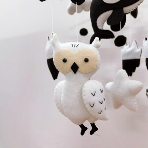 K&ouml;nnte beinhalten: Handgefertigtes Babymobile mit Filztierformen in Wei&szlig;, Schwarz und Beige. Das Mobile enth&auml;lt eine Eule, einen Orca und Sterne. Die Eule hat beige Augen und einen schwarzen Schnabel. Das Mobile ist an wei&szlig;en Schn&uuml;ren aufgeh&auml;ngt.