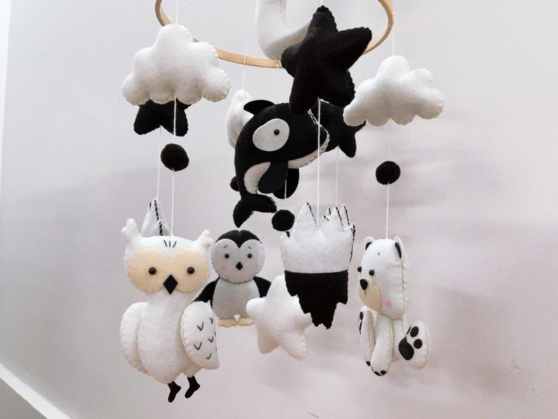 K&ouml;nnte beinhalten: Handgefertigtes Baby-Mobile mit Filztieren in Schwarz und Wei&szlig;. Das Mobile enth&auml;lt eine Eule, einen Pinguin, einen Eisb&auml;ren, einen Wal, Wolken, Sterne und eine Krone, die an einem Holzreifen aufgeh&auml;ngt sind.