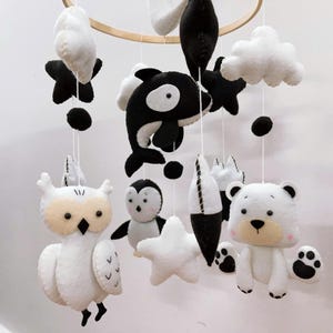 K&ouml;nnte beinhalten: Baby-Mobile mit Tierfiguren aus Filz in Schwarz und Wei&szlig;. Das Mobile umfasst eine Eule, einen Pinguin, einen B&auml;ren, einen Orca, Sterne, Wolken und abstrakte Formen, die an einem Holzreifen aufgeh&auml;ngt sind. Eine charmante Dekoration f&uuml;r das Kinderzimmer.
