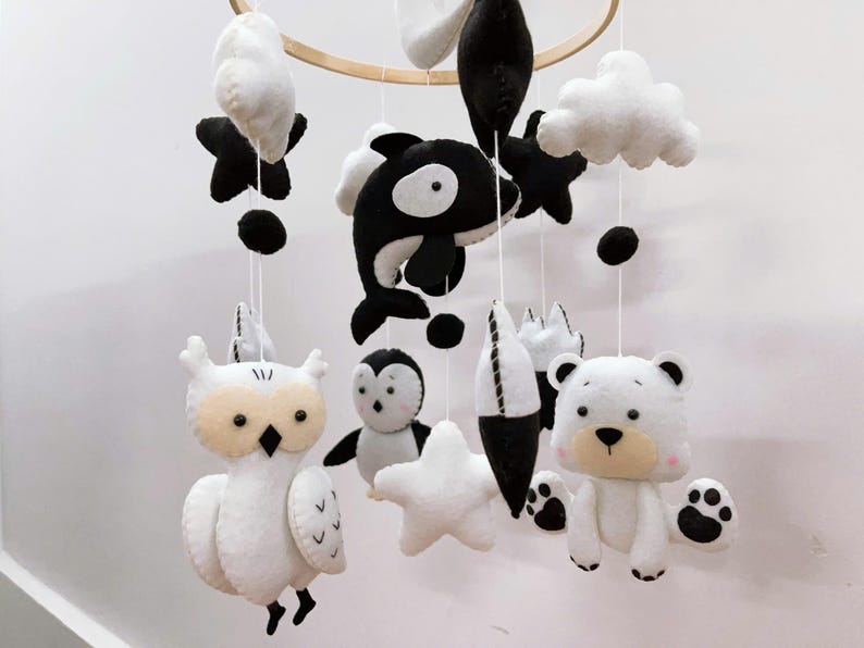 K&ouml;nnte beinhalten: Baby-Mobile mit Tierfiguren aus Filz in Schwarz und Wei&szlig;. Das Mobile umfasst eine Eule, einen Pinguin, einen B&auml;ren, einen Orca, Sterne, Wolken und abstrakte Formen, die an einem Holzreifen aufgeh&auml;ngt sind. Eine charmante Dekoration f&uuml;r das Kinderzimmer.