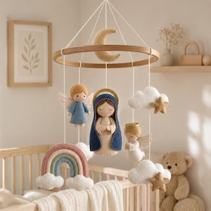 Puede incluir: Un móvil de cuna con marco circular de madera y figuras de fieltro colgantes, incluyendo una figura central de María con manto azul, dos ángeles con alas, una luna creciente, un arcoíris con nubes y dos estrellas sobre nubes blancas.