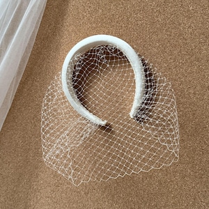 May include: A white bridal veil and a white headband with a net veil attached. The veil is made of a sheer, flowing fabric. The headband is covered in a smooth, white material. The net veil is a fine, delicate mesh.