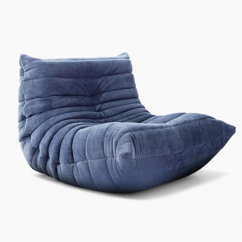 Puede incluir: Un sill&oacute;n lounge de pana azul con un perfil bajo y un dise&ntilde;o curvo &uacute;nico. La silla tiene una apariencia suave y acogedora, con crestas horizontales que crean una superficie texturizada. Dise&ntilde;ado para la comodidad y la relajaci&oacute;n.