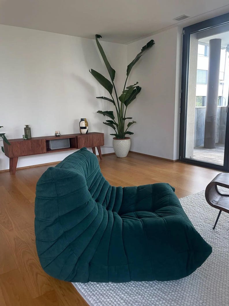 Puede incluir: Una taza de cer&aacute;mica blanca con un asa negra y el texto "But First, Coffee" en negrita negra. La taza se encuentra sobre un fondo borroso, sugiriendo un ambiente acogedor.