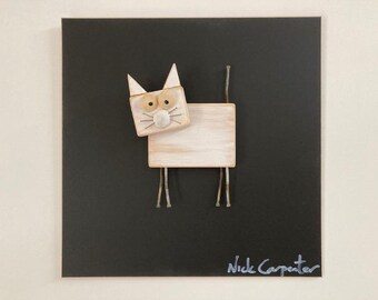 May include: Wooden cat art piece on a black square background. The cat is constructed from light-colored wood blocks with metal wire legs and tail. The artist's signature, "Nick Carpenter," is in the bottom right corner.
