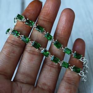 May include: A silver bracelet with rectangular, emerald-green gemstones. The gemstones are set in a row, connected by small silver links. The bracelet is displayed against a neutral background.