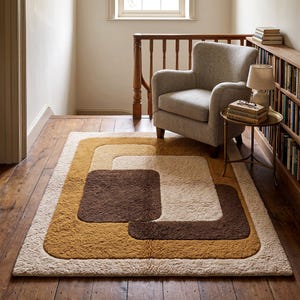 May include: A rectangular area rug featuring a geometric pattern of overlapping rounded squares in shades of dark brown, mustard yellow, and cream. The rug has a thick, textured pile construction and is positioned on a wooden floor surface.