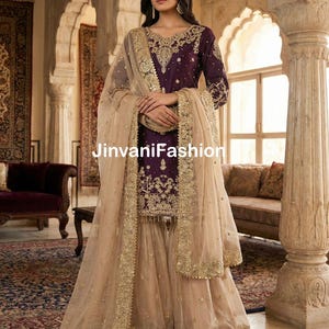 Puede incluir: Un traje Sharara formal, bordado en morado y dorado. El conjunto incluye una parte superior de manga larga, pantalones de pernera ancha y una dupatta transparente con ribete dorado. El texto "JinvaniFashion" es visible.