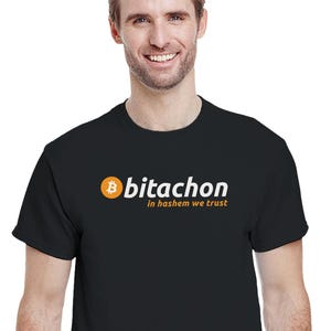 Può includere: T-shirt nera con la scritta "bitachon in hashem we trust". La parola "bitachon" è bianca e il logo Bitcoin è arancione. Il testo è centrato sul petto.