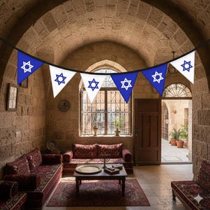 May include: A decorative string of pennant flags, with blue and white triangles, each displaying a Star of David. The flags are suspended in an arched room with stone walls, a window, and Middle Eastern furniture.