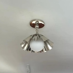 Peut inclure: Un plafonnier argenté avec un abat-jour festonné et une ampoule sphérique en verre blanc. Le luminaire est monté sur une base circulaire et possède une tige décorative. Design moderne et élégant.