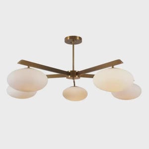 Peut inclure: Un plafonnier moderne avec une finition en laiton. Il comporte cinq bras s'étendant d'un moyeu central, chacun tenant un abat-jour en verre blanc de forme ovale. Le luminaire est conçu pour une utilisation en intérieur et fournit un éclairage ambiant.