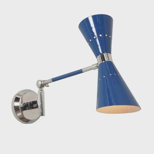 Peut inclure: Une applique murale dotée d'un abat-jour en forme de double cône bleu brillant avec de petits trous perforés. Le luminaire comprend une base circulaire en chrome poli, un bras réglable et une bande centrale chromée reliant les deux cônes.
