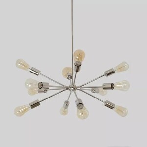Peut inclure: Un lustre moderne de style sputnik avec plusieurs bras s'étendant d'un moyeu central. Chaque bras contient une ampoule de style vintage avec une lueur ambrée chaude. Le luminaire est en métal poli et est suspendu à une seule tige.
