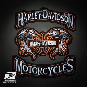 Puede incluir: Parches bordados de Harley-Davidson en negro, blanco y naranja. El diseño incluye el logotipo de Harley-Davidson, cabezas de águila y la palabra "MOTORCYCLES". Los parches son probablemente para chaquetas o chalecos.