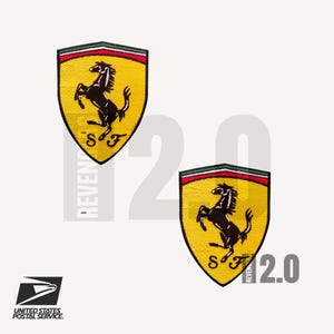 May include: Two yellow Ferrari patches with the iconic black prancing horse logo, red and green trim, and the letters "SF". The patches are set against a white background with the text "REVENGE 2.0". The United States Postal Service logo is in the lower left.