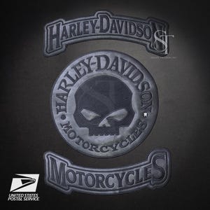 May include: Three dark grey Harley-Davidson patches. The top patch is arched with the brand name. The centre patch is circular with a skull and the brand name. The bottom patch reads "Motorcycles". The United States Postal Service logo is in the lower left.