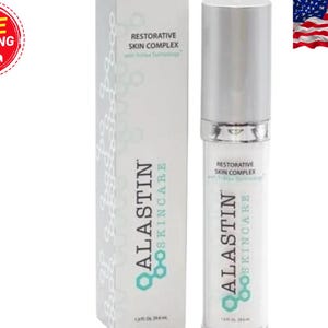 May include: A white and silver skincare product bottle and box. The bottle has a silver cap and the box has the text "ALASTIN SKINCARE" and "RESTORATIVE SKIN COMPLEX". The American flag is in the background.