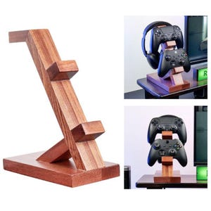 Könnte beinhalten: Ein brauner Gaming-Zubehörständer aus Holz mit rechteckiger Basis und einer abgewinkelten vertikalen Stütze mit zwei hervorstehenden Ablagen. Der Ständer ist zur Aufbewahrung von zwei Gaming-Controllern und einem Headset aus Holz gefertigt.