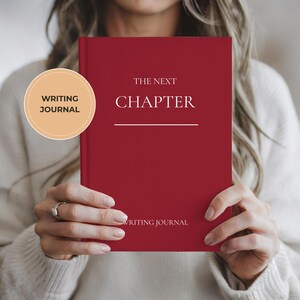 Peut inclure: Un journal d'écriture rouge avec les mots "THE NEXT CHAPTER" en blanc. Le journal est tenu devant une personne. Un autocollant circulaire sur la gauche indique "WRITING JOURNAL". Le bas du journal indique "WRITING JOURNAL".