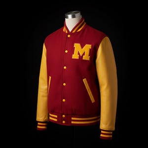 May include: A maroon and gold varsity jacket with a large yellow "M" patch. The jacket features yellow leather sleeves, a striped collar, cuffs, and hem. It has yellow buttons and two front pockets.