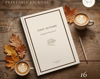 May include: A cream-colored journal with a dark brown border, featuring the text "COZY AUTUMN Reading & Writing Journal" and a line drawing of a coffee cup. It is accompanied by two cups of latte art, a pen, and several dried autumn leaves.