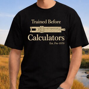 Puede incluir: Camiseta negra con el texto "Trained Before Calculators" y un gráfico de una regla de cálculo. El texto "Est. Pre-1970" está debajo de la palabra "Calculators". La camiseta tiene cuello redondo.
