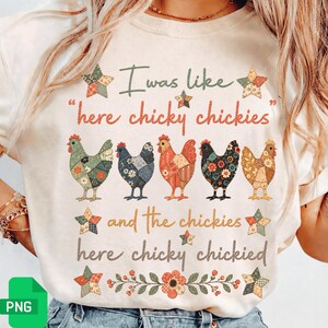May include: Cream-colored t-shirt featuring the text "I was like 'here chicky chickies' and the chickies here chicky chickied." The shirt has a graphic of five colorful chickens and star accents. Floral and leaf accents are at the bottom.