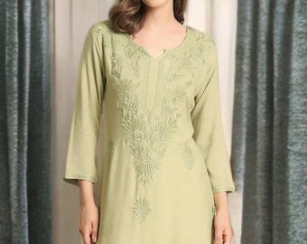 May include: A light green tunic with intricate embroidered floral patterns, paired with white palazzo pants. The tunic features a V-neck and three-quarter sleeves. The outfit is completed with white heeled sandals, creating a stylish and comfortable ensemble.