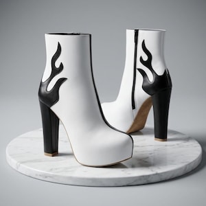 May include: White ankle boots with black flame designs on the sides and black block heels. The boots have a platform sole and a zipper closure. The boots are displayed on a marble surface.