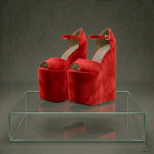Könnte beinhalten: Ein Paar leuchtend rote Plateausandalen mit offenem Zehenbereich. Die Schuhe haben eine dicke, rechteckige Plattform und einen Knöchelriemen mit Schnalle. Die Sandalen sind aus weichem, samtigem Material.